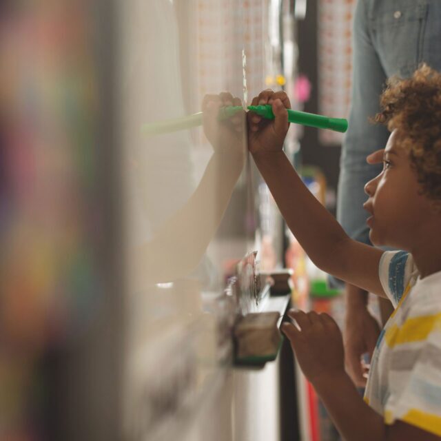 Elementary school student with a green highlighter on a whiteboard