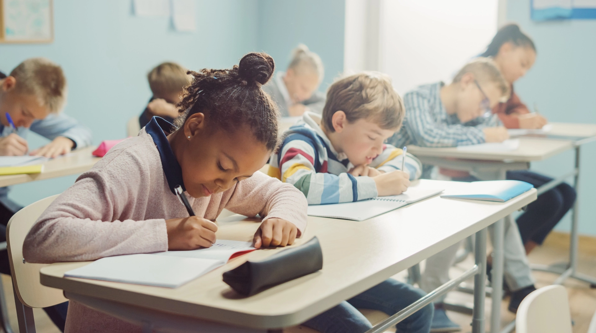 Young students writing in notebooks while seated at desks in a classroom