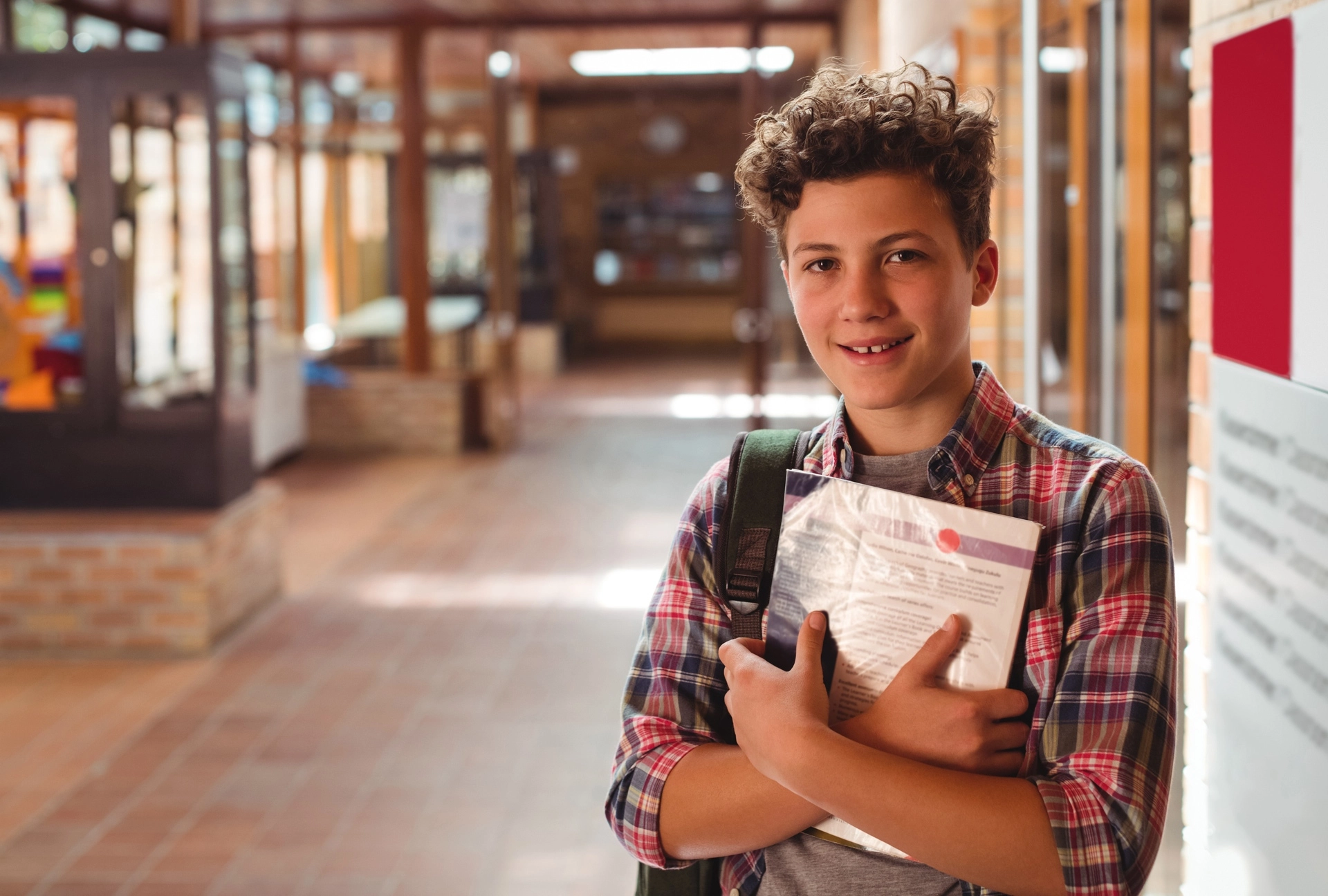 Student holding a textbook while standing in a school hallway