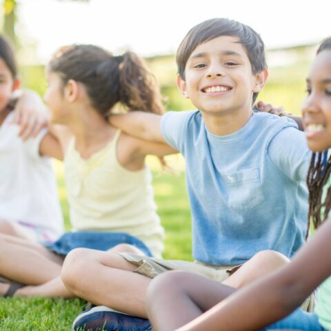 Group of smiling young students sitting outside on grass