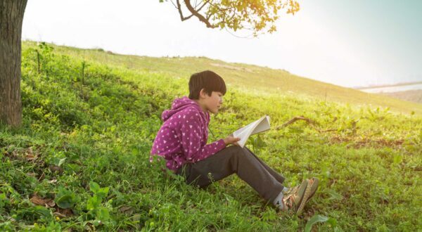 Student sits outside under a tree reading a book