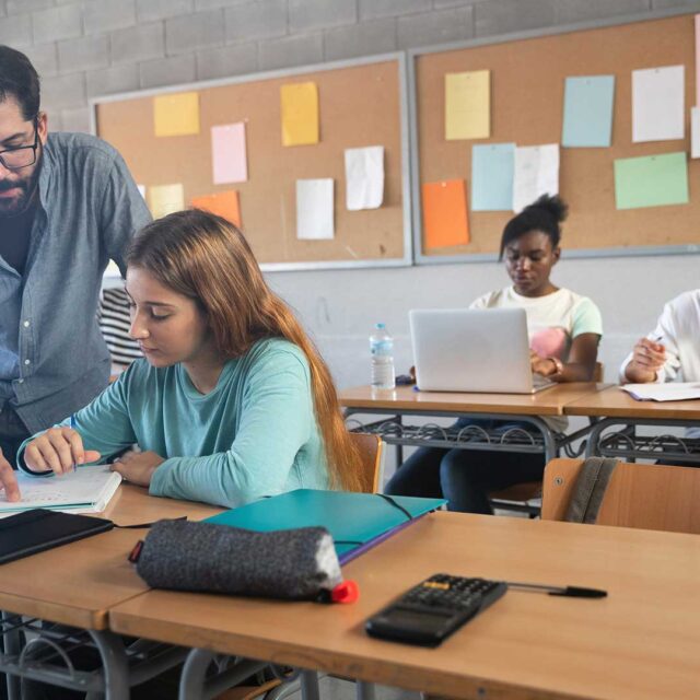 A teacher works with a high school student in a classroom.