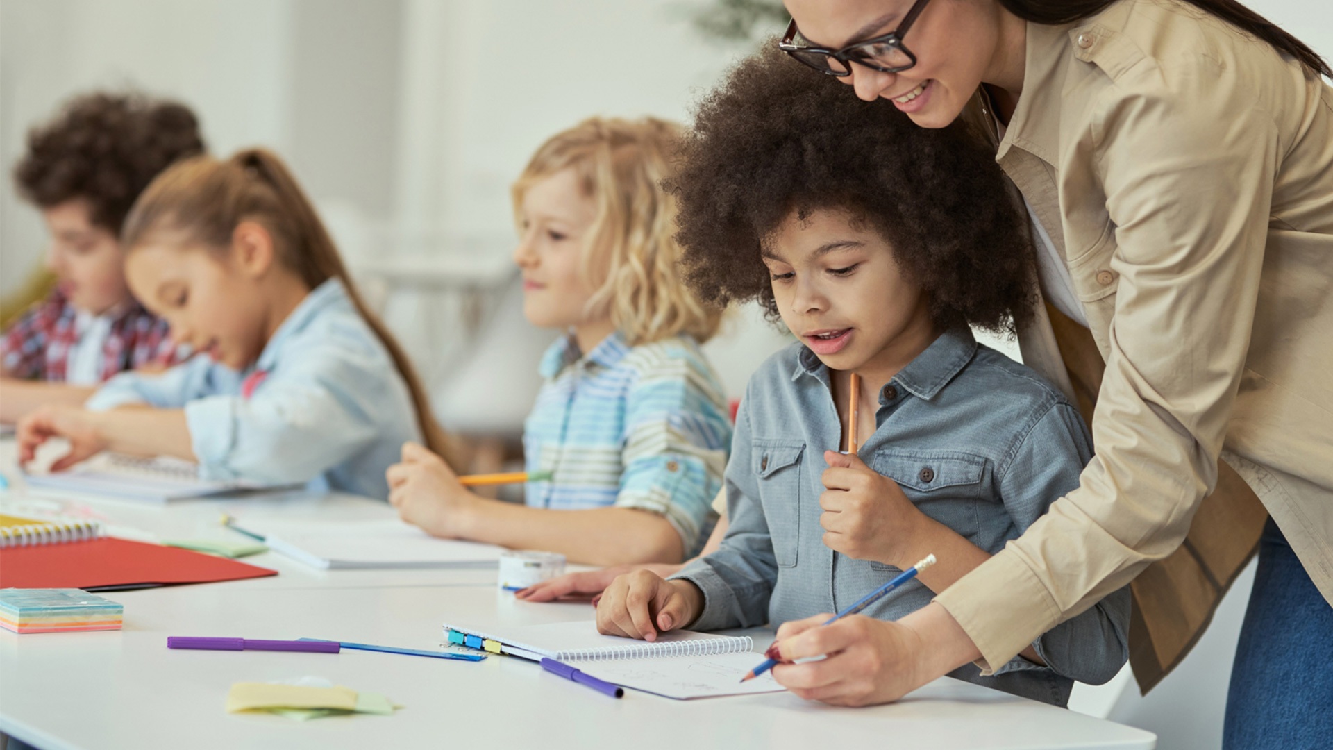 Kids working at desk with teacher leaning over them