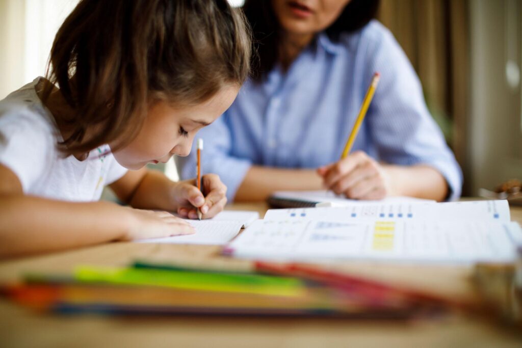 young girl at desk writing with teacher watching