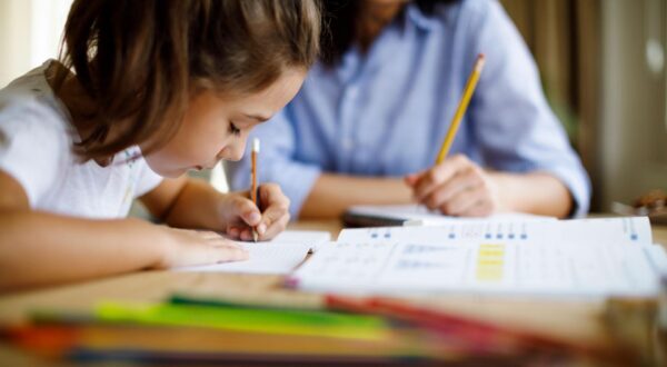 young girl at desk writing with teacher watching