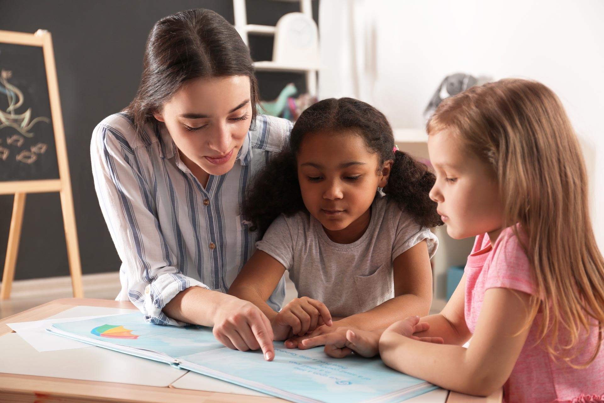 teacher pointing to book with two girls