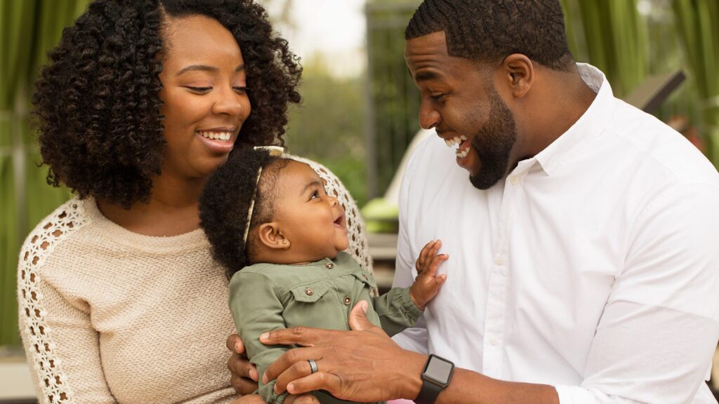 A mother and father hold a baby and engage the baby in talking and playing with sounds.