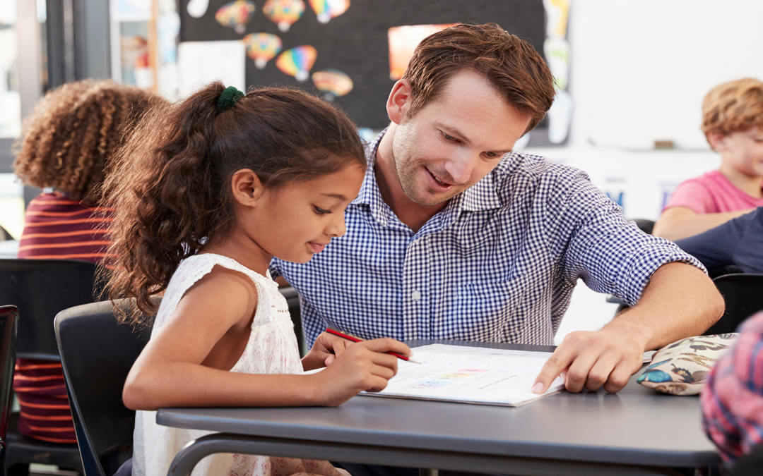 Male teacher working with student at desk.