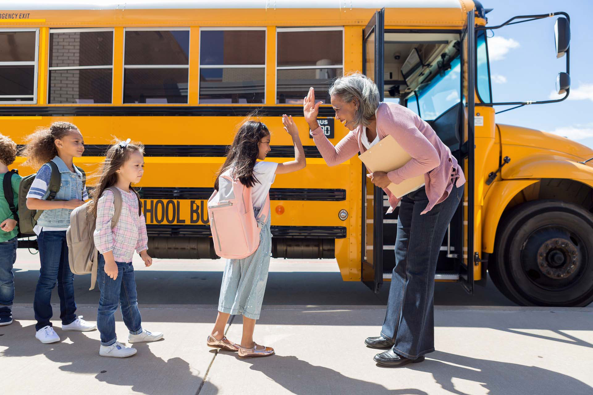 Principal of an elementary school giving a high-five to a student who is about to board a school bus