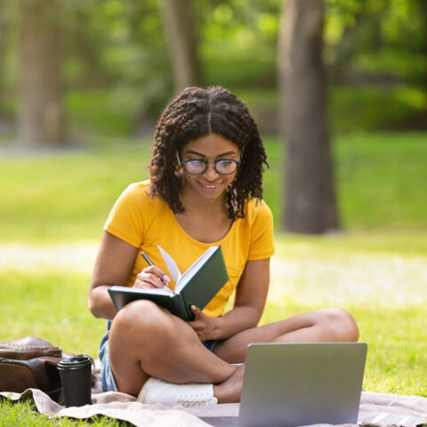 A young Black teenager reads outside in the summer