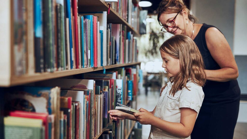 A teacher helps a child pick out a book at a school library.