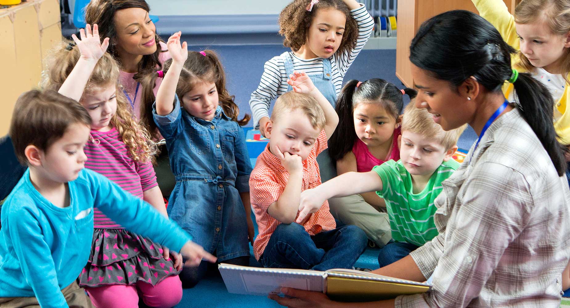 A preschool teacher reads a book to a group of young children.