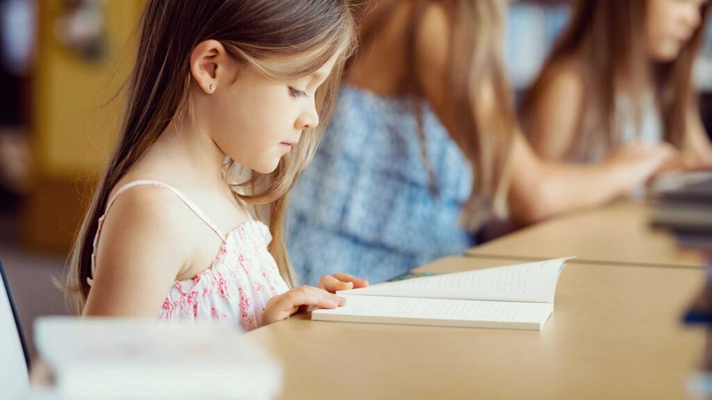An elementary student reads a book in class.