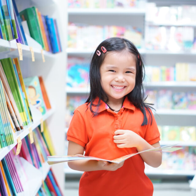 Smiling young child holding an open book in a library