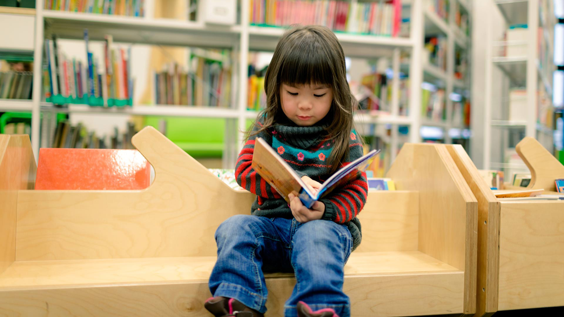 A young child looks through an open book in a library.
