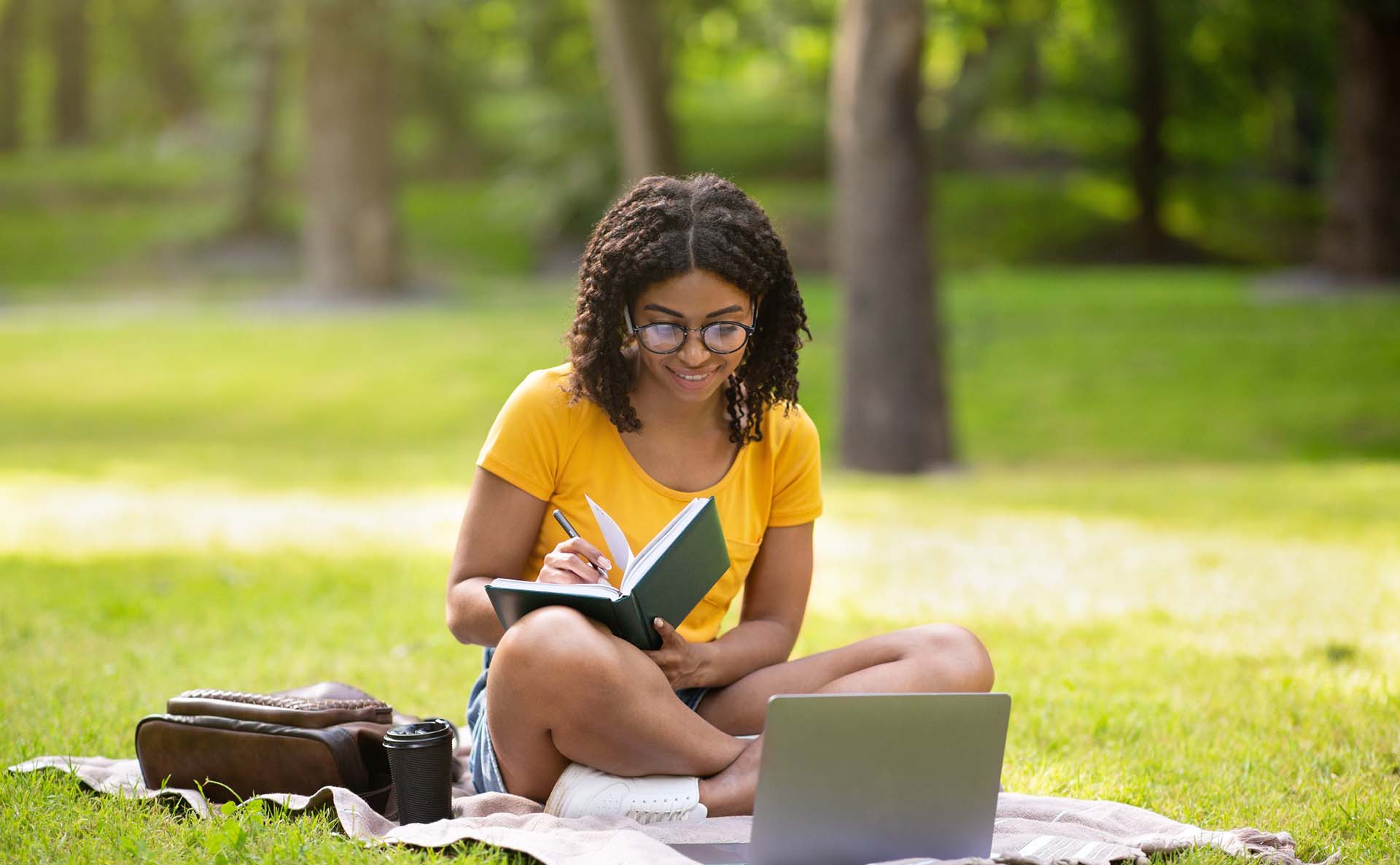 A young black teenager reads outside in the summer
