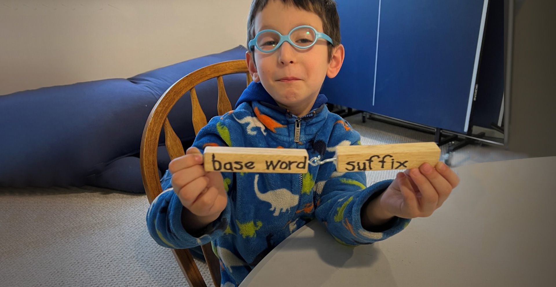 Student holds two connected wooden blocks. The first one says “base word” and the second says “suffix”