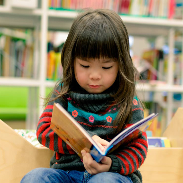 Preschool-age child looks through a book in a library.
