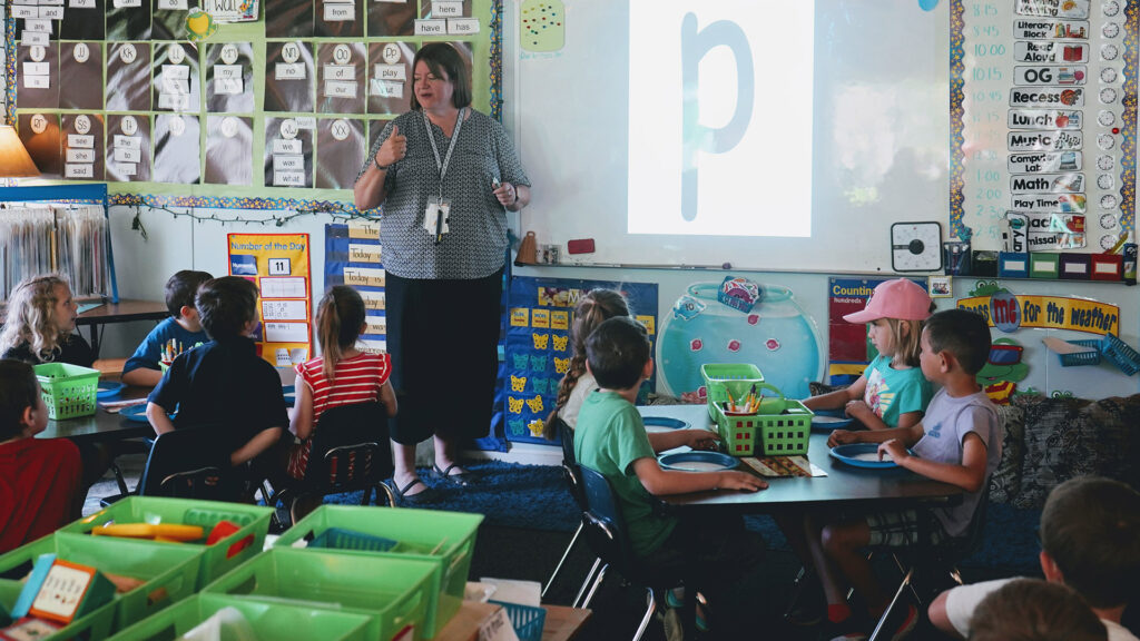 A teacher stands at the front of a kindergarten class, teaching the students how to identify and sound out the letter P.