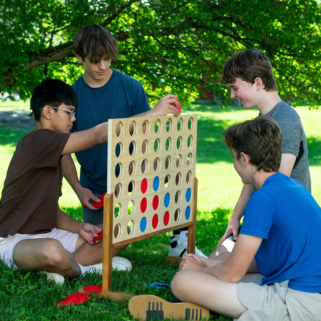 Four boys play a game of Connect Four outside.