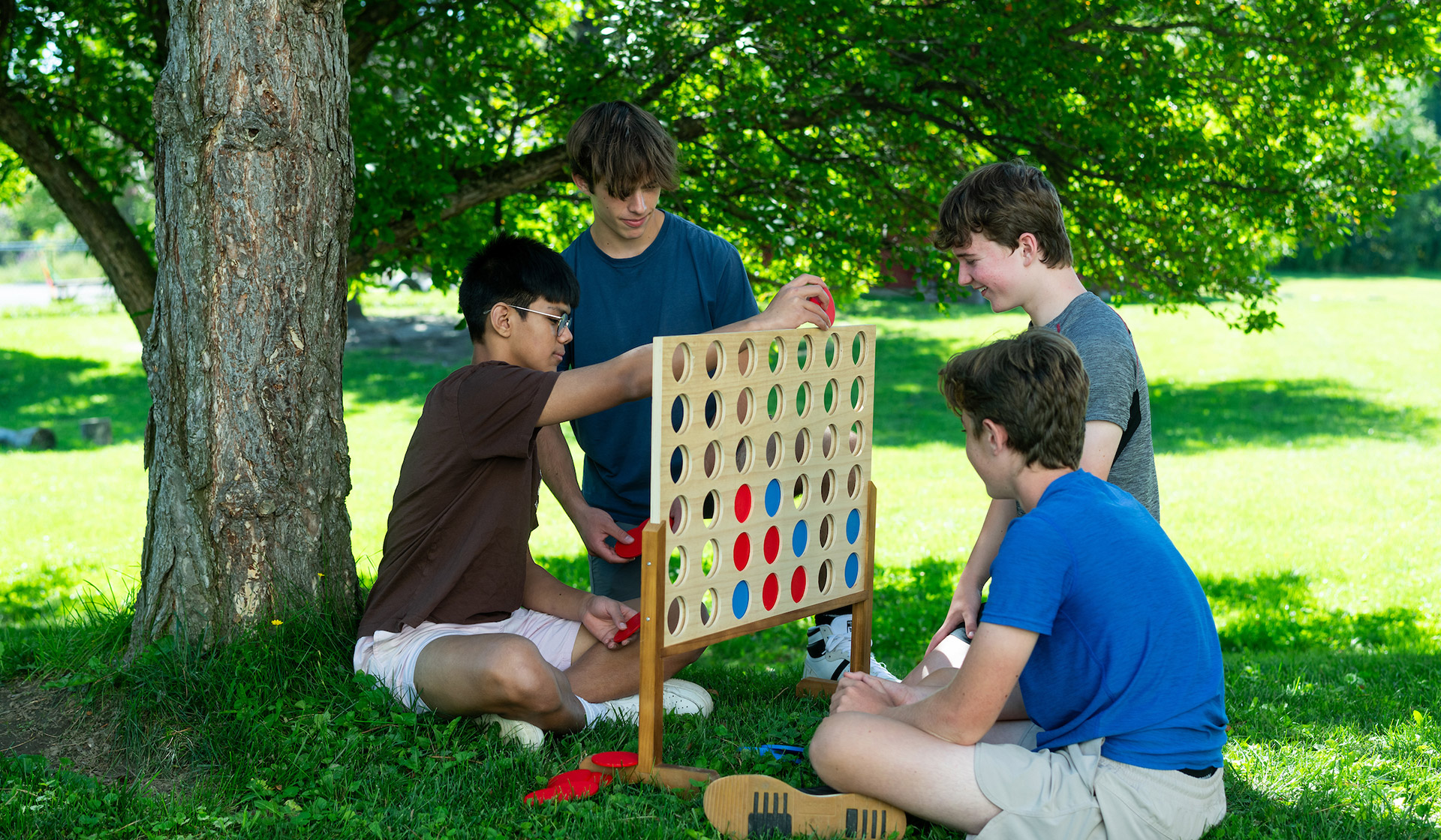 Four middle school boys play Connect Four outside.
