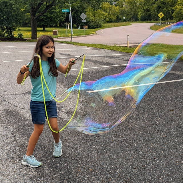 A student creates a huge soap bubble as part of a social learning summer camp.