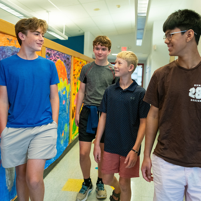 A group of four students walks down a hallway in a school.