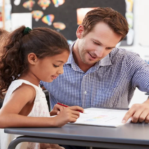 Male teacher working with student at desk.